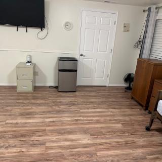 A tidy room with wooden flooring, featuring a mounted television, a small cabinet, and a door.