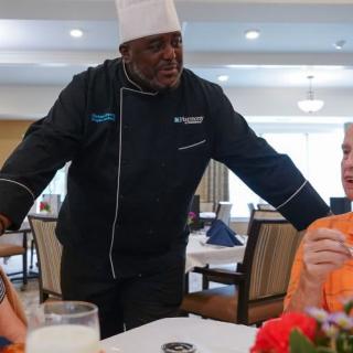 A chef engages in conversation with diners at a restaurant.