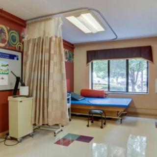 A hospital patient room with a bed and medical equipment, separated by a curtain, featuring a window for natural light.