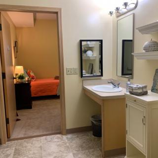 A view from a bathroom into a bedroom with warm lighting and simple decor.