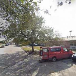 A red van parked in a lot beside a tree and a building.