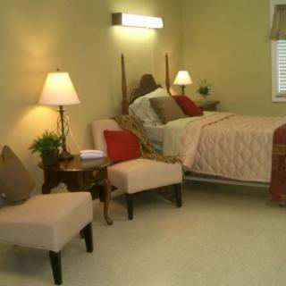 A cozy bedroom with a bed, two chairs, and soft lighting.