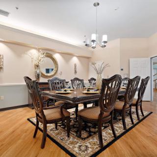 An elegant dining room with a large wooden table, surrounded by chairs and illuminated by a chandelier.