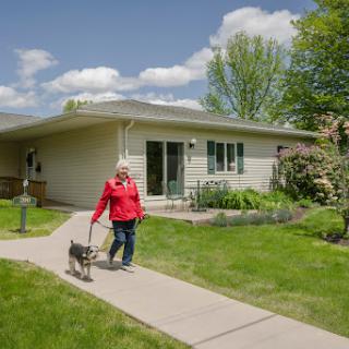A woman walking her dog along a pathway in front of her house on a sunny day.