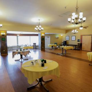 A spacious dining area with round tables, elegant chandeliers, and wooden flooring.
