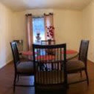 A cozy dining room with a round table and four chairs, accented by curtains and simple decor.
