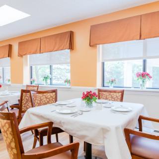 A bright and well-lit dining room with elegantly set tables, adorned with flowers.