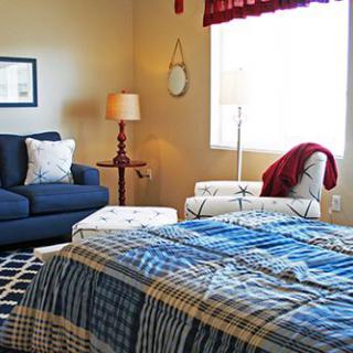 A cozy bedroom with a plaid-covered bed, sofa, and warm lighting.
