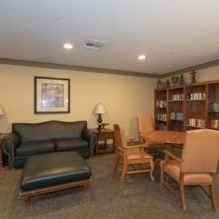 A cozy living room featuring a black sofa, ottoman, wooden table with chairs, bookshelf and lamps.