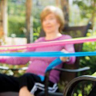 An elderly woman exercising with resistance bands outdoors.