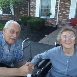 An elderly couple enjoying time outdoors in front of a brick building.