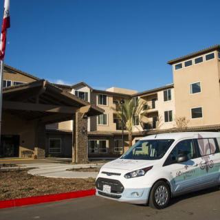 A white van parked in front of a multi-story building with an American flag nearby.