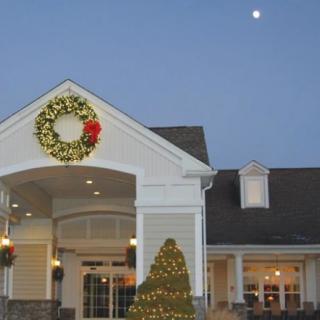 A festively decorated building with a large wreath and Christmas tree, set against an evening sky.