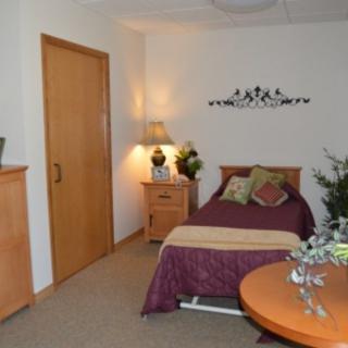 A cozy bedroom featuring a single bed with pillows, a nightstand with a lamp, and decorative elements.