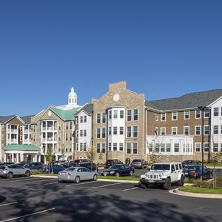 A multi-story residential complex with a large parking area on a clear, sunny day.