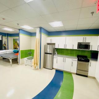 A brightly designed kitchen area within a medical facility, featuring stainless steel appliances and vibrant green and blue accents.