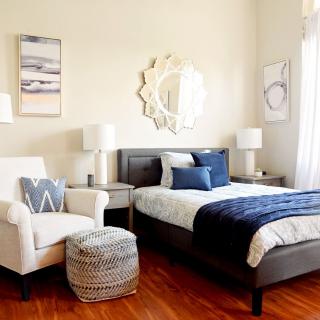 A cozy and stylish bedroom featuring a large bed with blue accents, an inviting armchair, decorative mirrors, and elegant lighting.