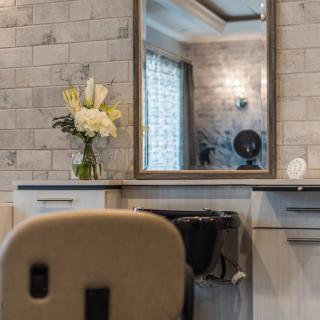 A stylish salon interior featuring a large mirror, floral arrangement, and comfortable chair.