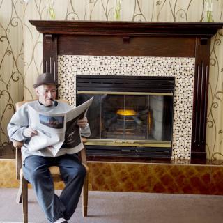 A person sitting by the fireplace reading a newspaper.
