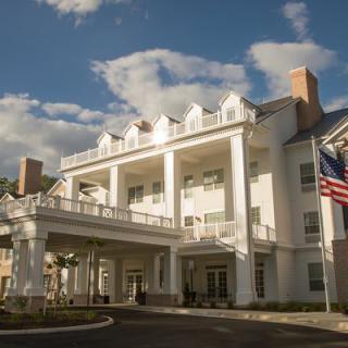 Elegant colonial-style building with white pillars and flags against a backdrop of a partly cloudy sky.