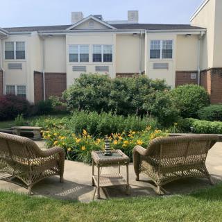 A serene garden seating area with wicker chairs and lush greenery in front of a residential building.