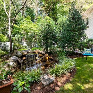 A serene garden scene featuring a small waterfall surrounded by lush greenery and a seating area.