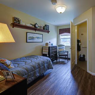A cozy bedroom featuring a single bed, a stylish lamp, and warm decor.