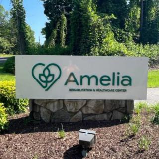 Sign for Amelia Healthcare Facility surrounded by greenery.