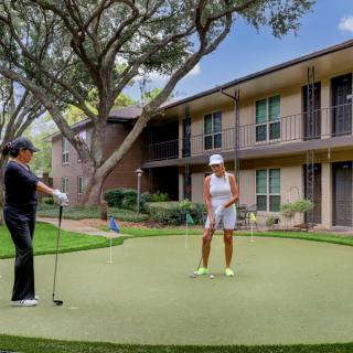 Two people playing golf on a putting green in an apartment complex.