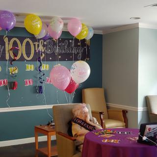 A room decorated for a birthday celebration with colorful balloons and a banner.
