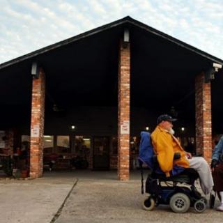 A person in a wheelchair is positioned outside a brick building with an open entrance.