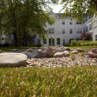 A scenic view of a building surrounded by a garden with stones and greenery.