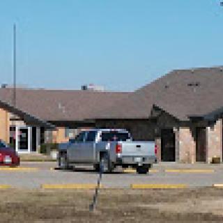 A parking lot view featuring a silver pickup truck and a red car in front of a brick building.