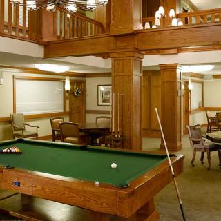 A cozy lounge area featuring a billiards table with rich wood paneling and elegant chandeliers.