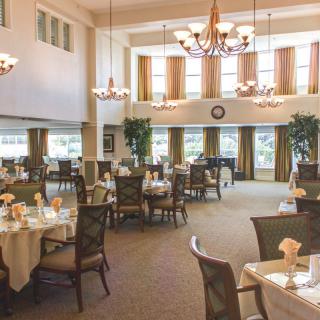 An elegant dining room with chandeliers and set tables, featuring large windows.