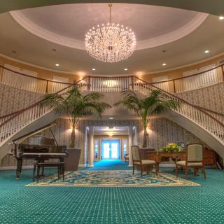 A luxurious hotel lobby featuring a grand staircase, chandelier, and piano.