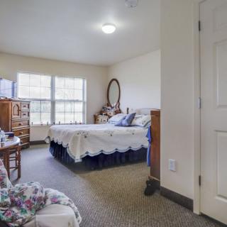 A cozy bedroom with a large window, bed, and wooden furniture.
