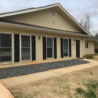 A charming single-story house with yellow siding and black shutters, featuring a neatly landscaped front area.