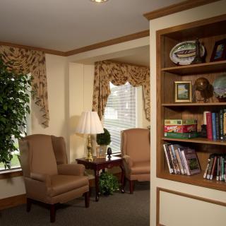 A cozy living room with armchairs, a lamp, and a bookshelf.