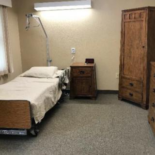 A simple hospital room with a bed and wooden furniture.
