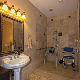 A modern, handicap-accessible bathroom featuring a sink, mirror, and shower area with tiled walls.