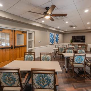 A well-appointed meeting room with tables, decorated chairs, a television, and ceiling fan.