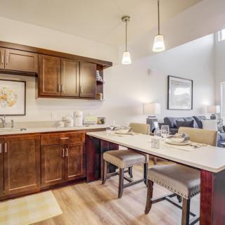 A modern kitchen with a dining area featuring wooden cabinets, bar stools, and pendant lighting.