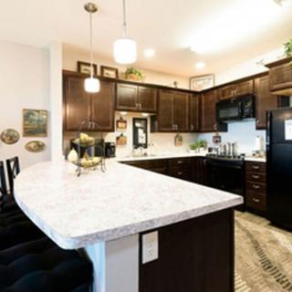 A modern kitchen with dark cabinets and a spacious white countertop, featuring pendant lighting and various appliances.