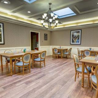 A cozy dining room with wooden tables and chairs, illuminated by a chandelier and natural light from skylights.