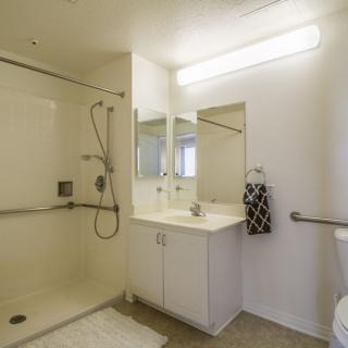 A modern, minimalist bathroom featuring a spacious shower and a sleek white vanity with a mirror.