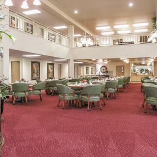 A spacious dining area with red carpet, green chairs, and ample lighting.
