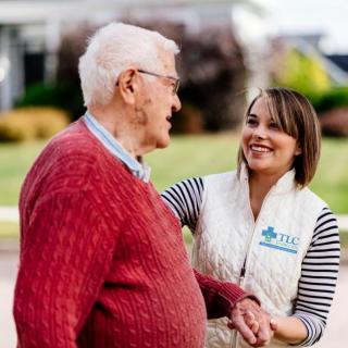 A caregiver smiling and interacting with an elderly man outdoors.