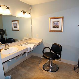 A well-lit bathroom vanity area with a mirror, chair, and sink.