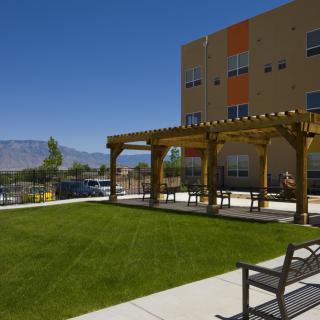 A modern building with an outdoor patio featuring a pergola and a well-maintained lawn under a clear blue sky.